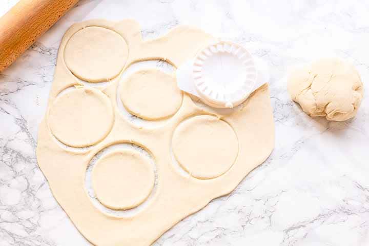 Roll out the empanada dough on a lightly floured surface to prevent sticking. Use a round cutter or a bowl to cut out circles.