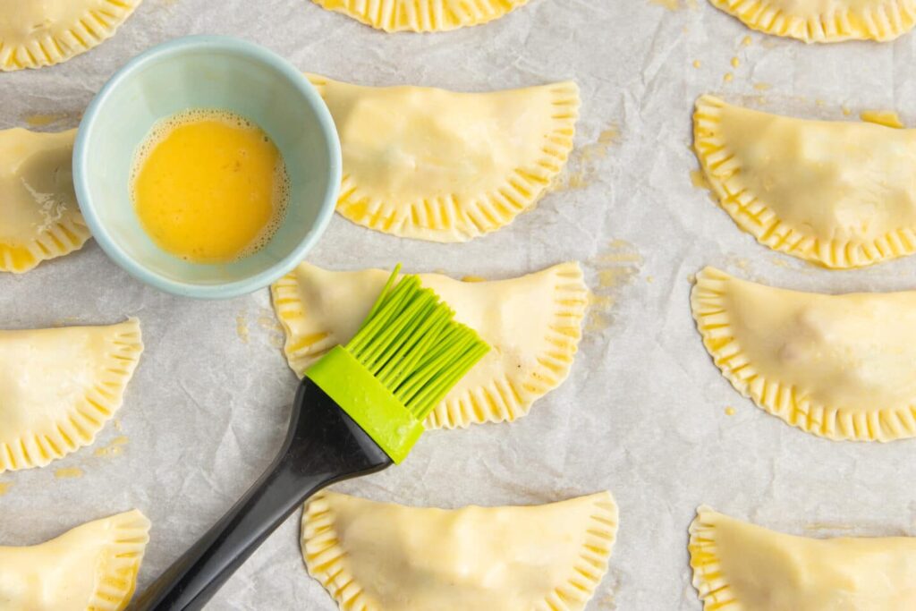 Beat an egg in a small bowl and brush the top of each empanada with the egg wash